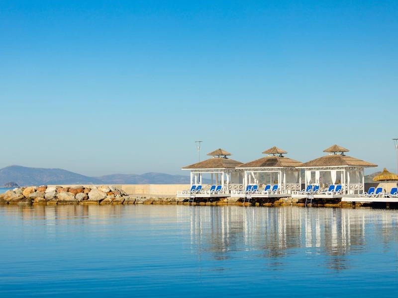 Three beach huts with loungers by calm sea under clear blue sky.