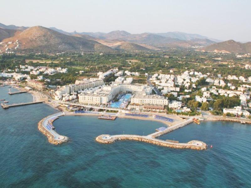 Aerial view of a coastal town with harbor, beaches, and mountains in the background.