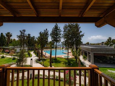 Vue depuis le balcon sur une piscine, des arbres et des chemins dans un complexe hôtelier par temps ensoleillé.