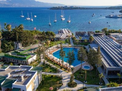 Luxuriöse Hotelanlage mit Pools, grünen Gärten und Blick auf das blaue Meer mit Segelbooten.