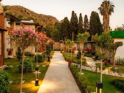 Un sentier de jardin bien entretenu entre des bâtiments avec des arbres et des arbustes au coucher du soleil.