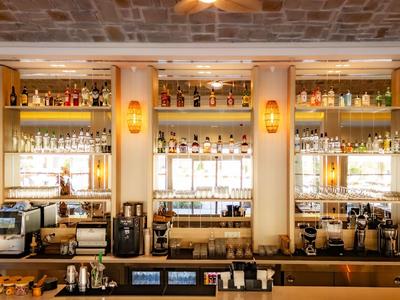 Bar moderne avec comptoir en bois, étagères éclairées et machines à café dans un hôtel.