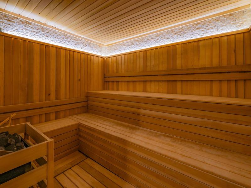 Sauna avec bancs en bois à plusieurs niveaux et éclairage indirect au plafond.
