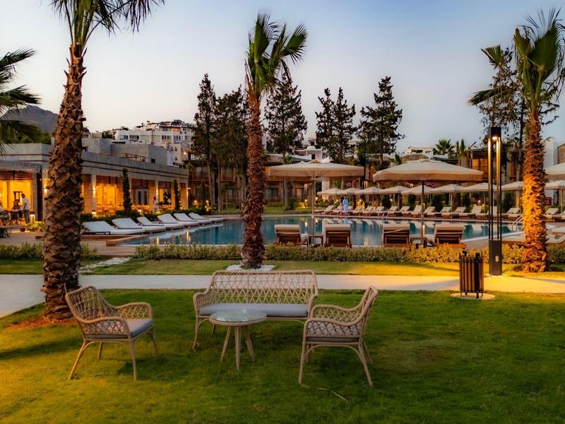 Vue du soir d'un hôtel avec bungalows éclairés, piscine et palmiers.