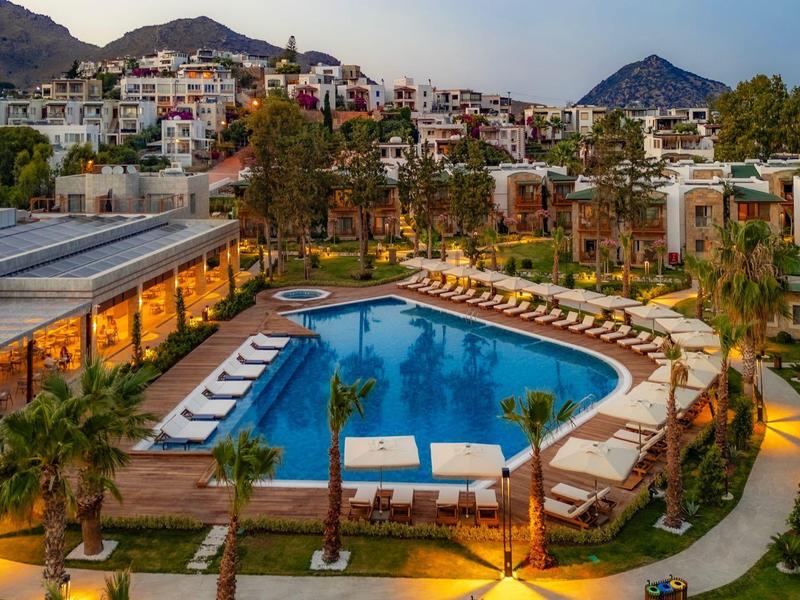 Complexe hôtelier avec piscine éclairée et chaises longues dans un paysage montagneux au crépuscule.