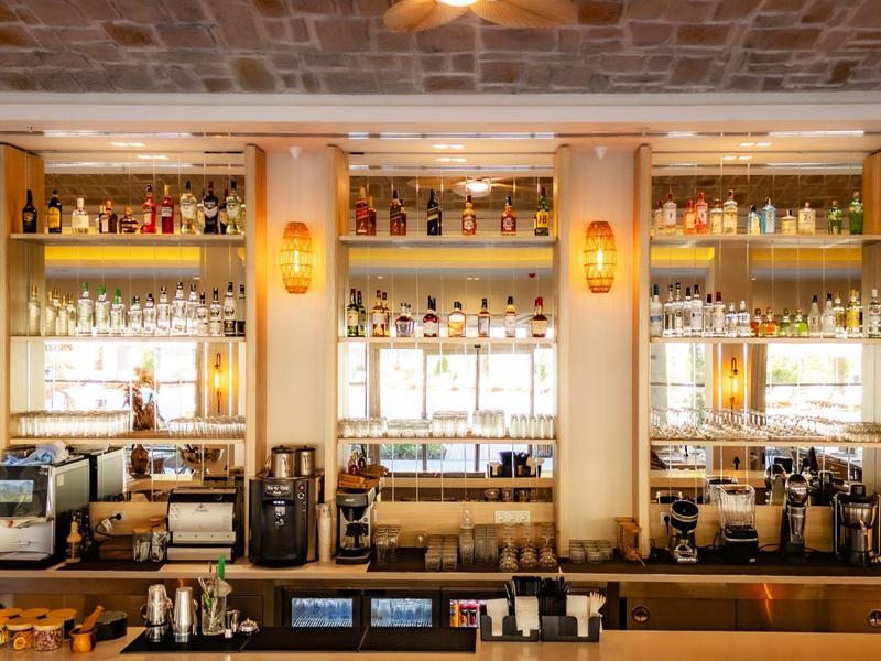 Bar moderne avec comptoir en bois, étagères éclairées et machines à café dans un hôtel.