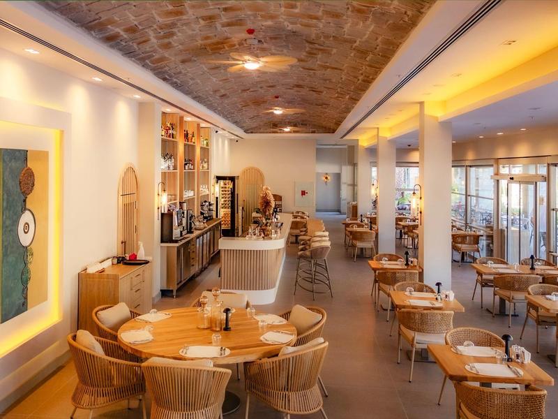 Restaurant d'hôtel lumineux et accueillant avec chaises en bois et rotin, éclairage chaleureux et plafond décoratif.