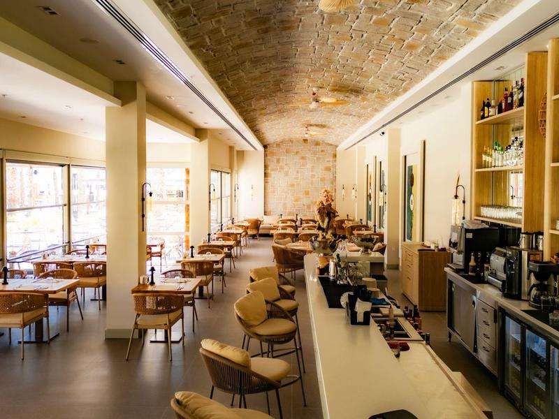 Restaurant moderne et lumineux avec grandes tables, bar, grandes fenêtres et plafond élégant.