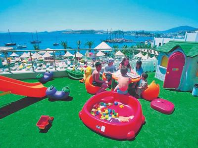 Spielplatz mit buntem Kunststoffspielzeug, Rutsche und Liegestühlen am Meer bei sonnigem Wetter.