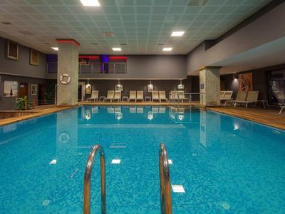 Innenpool mit klar blauem Wasser, Edelstahlgeländer, Liegestühlen und ruhiger Beleuchtung.