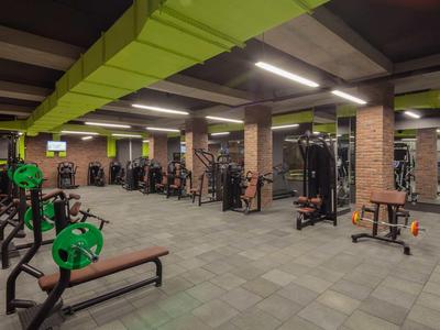 Salle de sport moderne avec équipements de musculation et accents verts au plafond dans un hôtel.