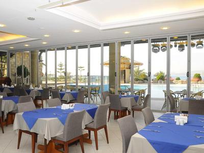 Moderner Speisesaal mit blauen Tischdecken, Holzstühlen und großen Glasfenstern zum Außenbereich.