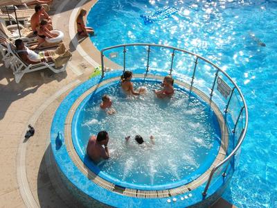 Mehrere Personen entspannen in einem runden Whirlpool neben einem blauen Schwimmbecken.