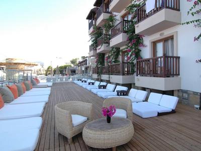 Moderne Hotelterrasse mit Holzdeck, weißen Liegen, Stühlen und Blumendekoration.