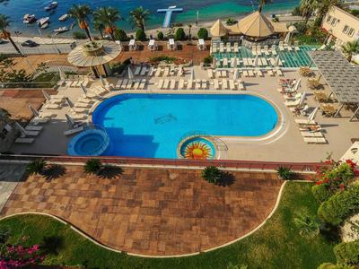 Großer blauer Pool mit Sonnenschirmen und Liegestühlen, umgeben von Sandstrand und Palmen.