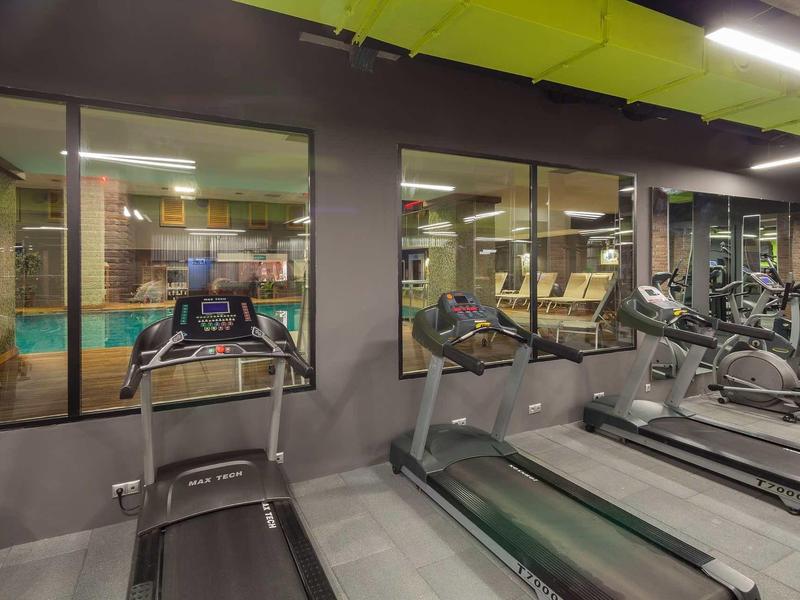 Moderner Fitnessraum mit grüner Decke, Laufbändern und Spiegelwand gegenüber.