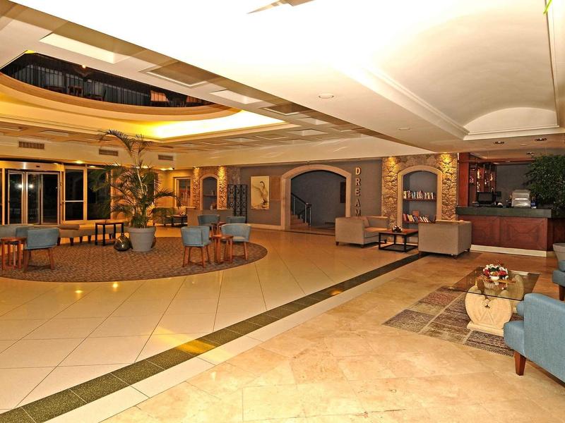 Große Lobby mit warmem Licht, runden Sitzbereichen, Pflanzen und Marmorboden.