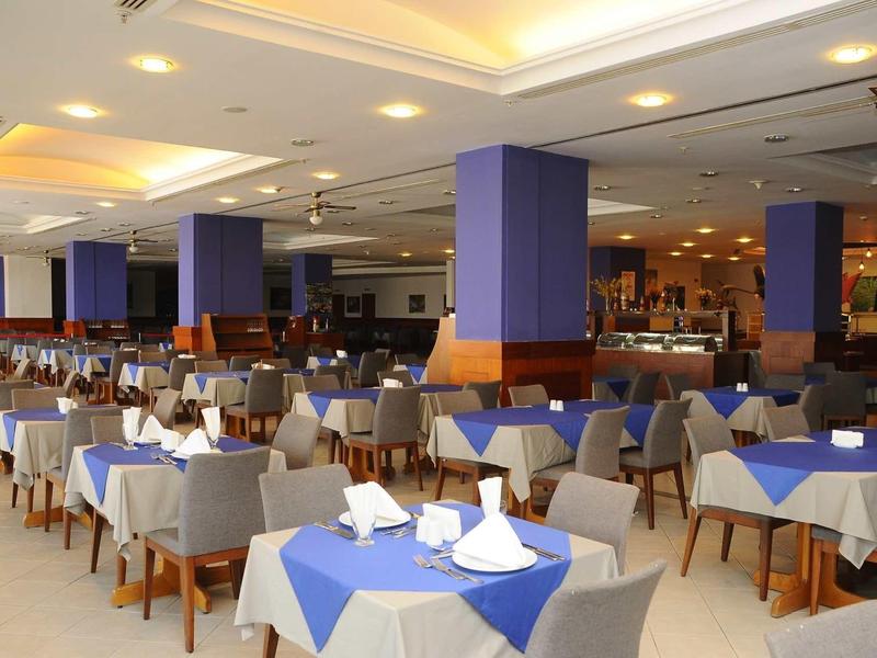 Großer, heller Speisesaal mit vielen Tischen, blau-weißen Tischdecken und gedeckten Plätzen.