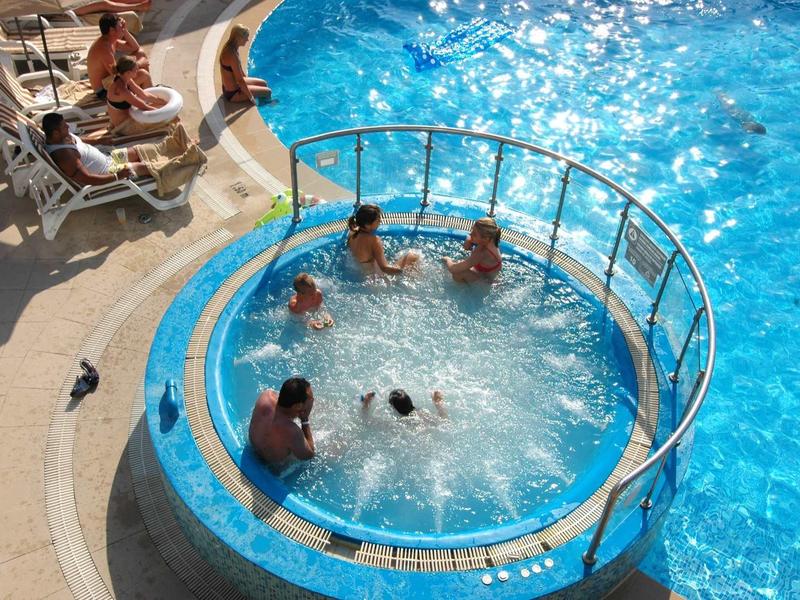 Mehrere Personen entspannen in einem runden Whirlpool neben einem blauen Schwimmbecken.