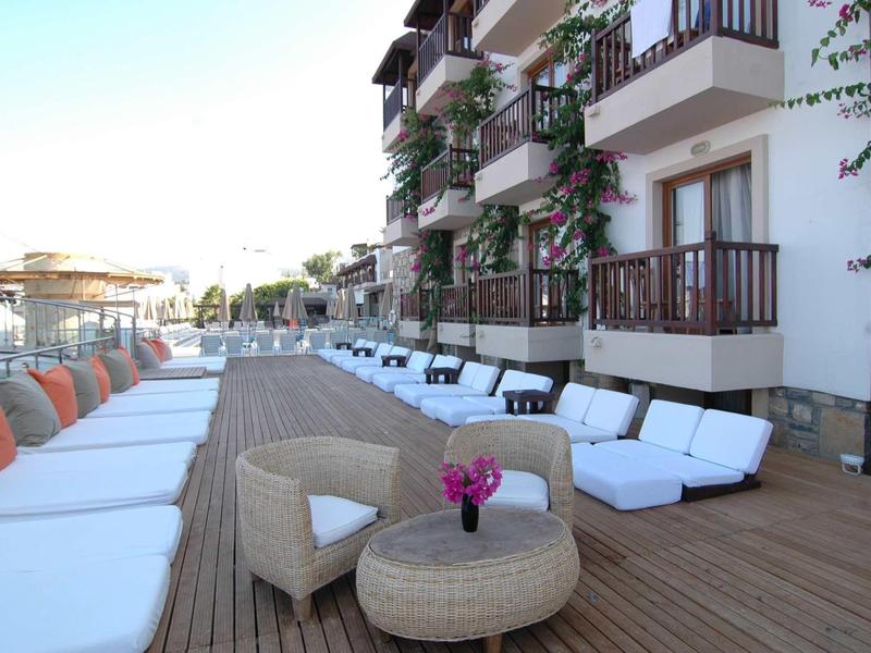 Moderne Hotelterrasse mit Holzdeck, weißen Liegen, Stühlen und Blumendekoration.