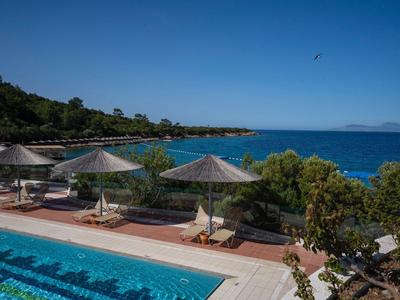 Area piscina con ombrelloni e lettini vicino al mare e a una riva alberata
