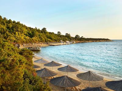 Beach with wooden walkways, straw umbrellas, and clear blue water at sunset.
