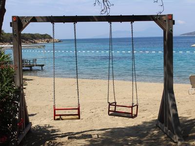 Two swing seats on a wooden frame at a sandy beach overlooking the blue sea.