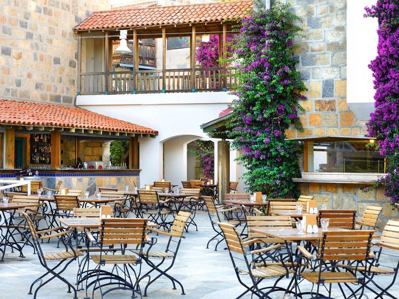 Quiet outdoor seating area with wooden tables and chairs by a stone wall with flowers at the hotel.