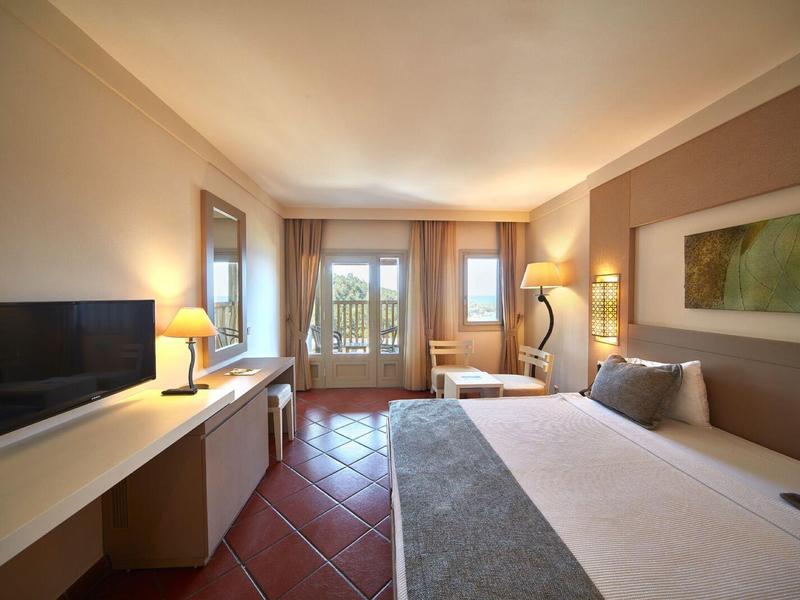 Cozy hotel room with large bed, TV, desk, and balcony with outdoor view.