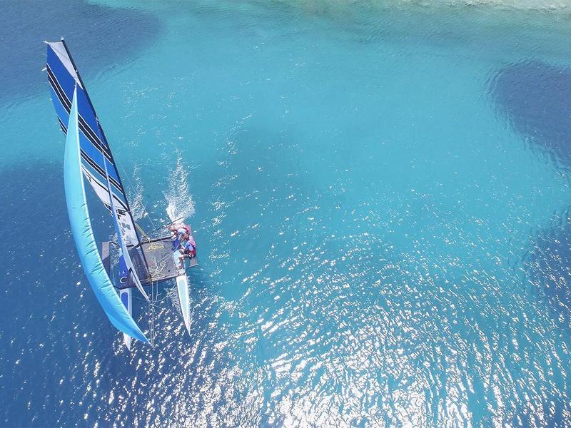 Sailboat with blue sail on clear blue water in sunny weather
