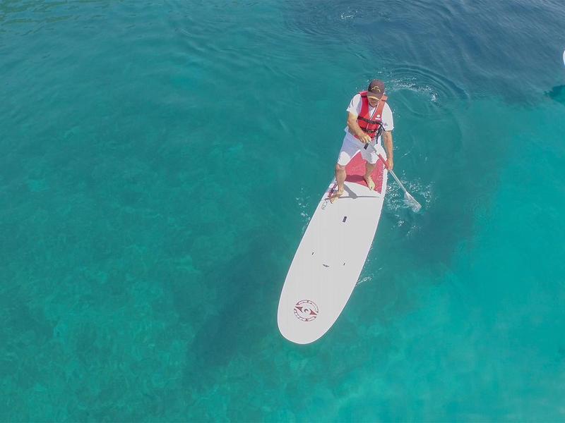 Woman on a stand-up paddleboard on clear turquoise water next to other paddleboards.