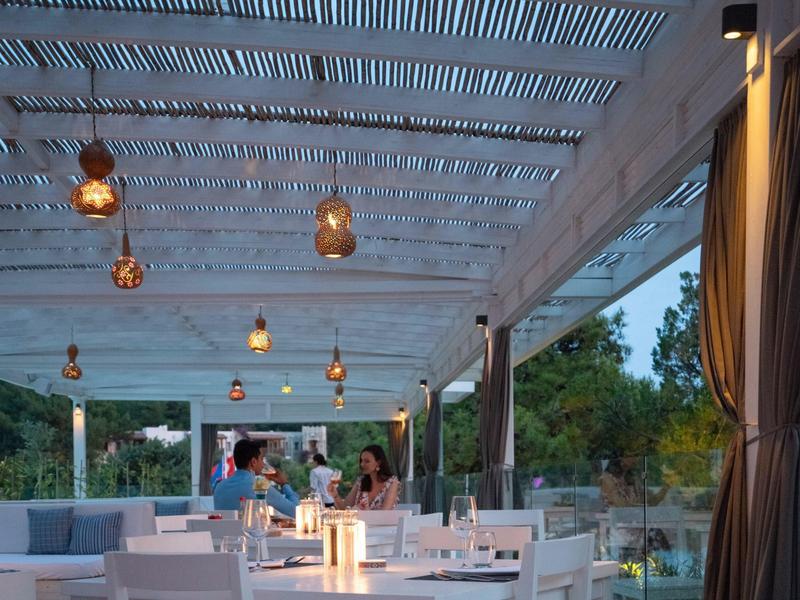 Cozy terrace with white furniture and decorative lighting in a hotel restaurant at dusk.