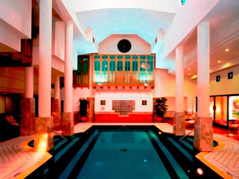 Indoor hotel pool with tall columns and bright lighting.