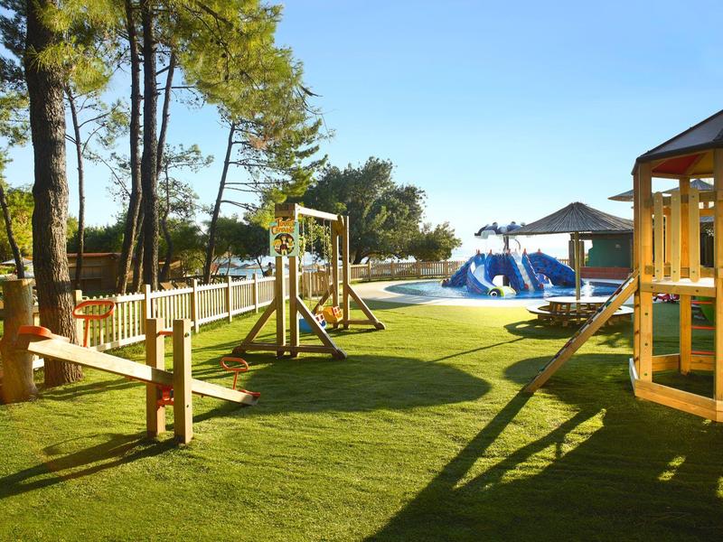 Children's playground with swings, climbing frames, and grass under a clear blue sky