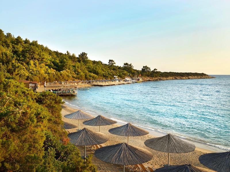 Beach with wooden walkways, straw umbrellas, and clear blue water at sunset.
