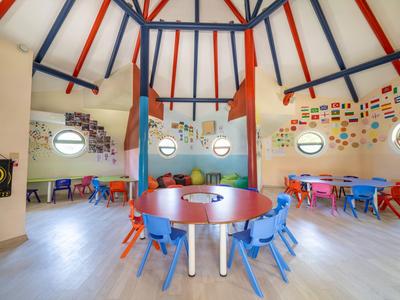 Sala de juegos colorida con mesas redondas y sillas pequeñas bajo techos altos de madera.