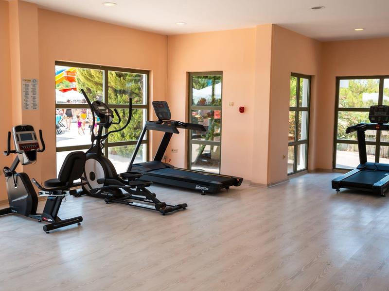 Hell eingerichteter Fitnessraum mit Laufbändern, Crosstrainern und großen Fenstern.