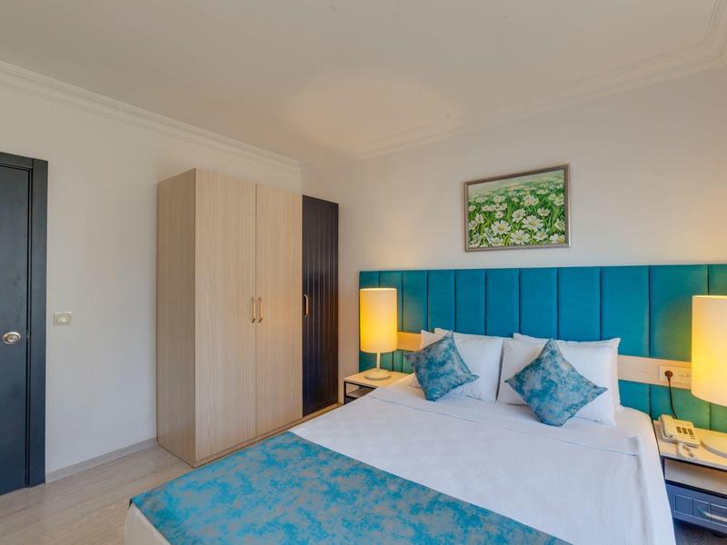 Helles Schlafzimmer mit großem Bett, türkisen Akzenten, Holzschrank und zwei Nachttischlampen.