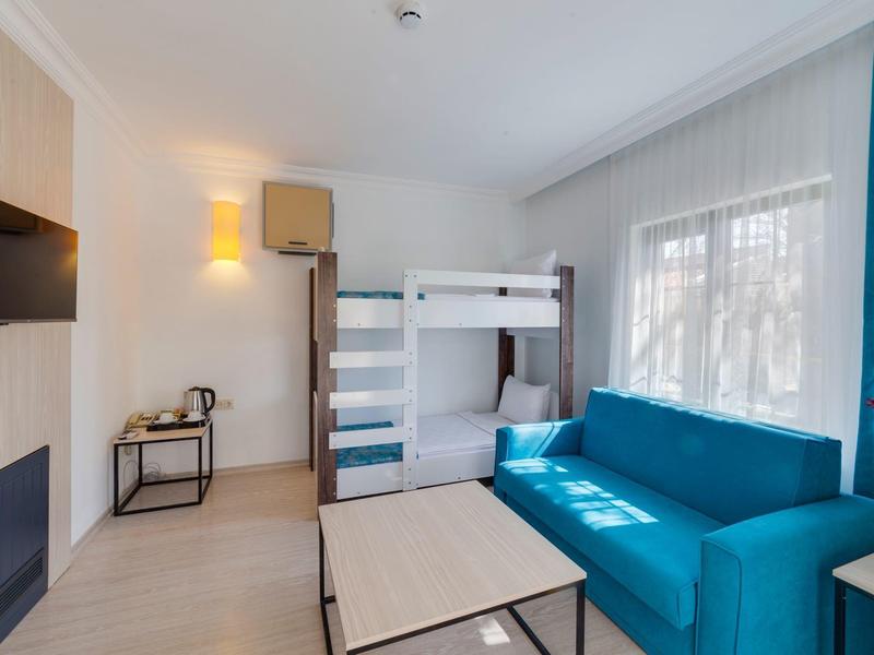 Kleines Zimmer mit Etagenbett, blauem Sofa, Fenster, Tisch und Wandhalterung für Fernseher.