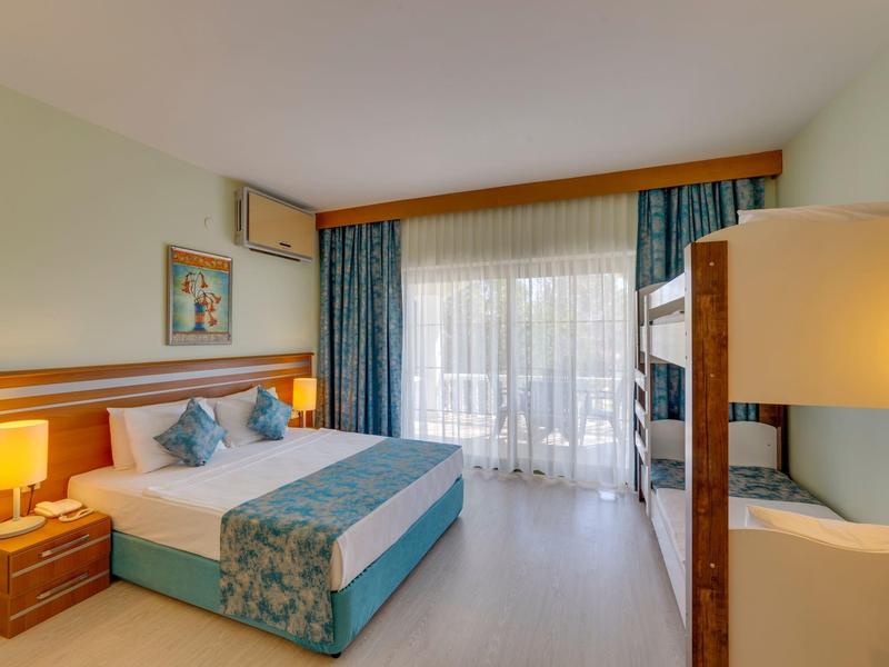 Gemütliches Hotelzimmer mit Doppelbett, Etagenbett, hellen Wänden, Lampen und großen Fenstern.