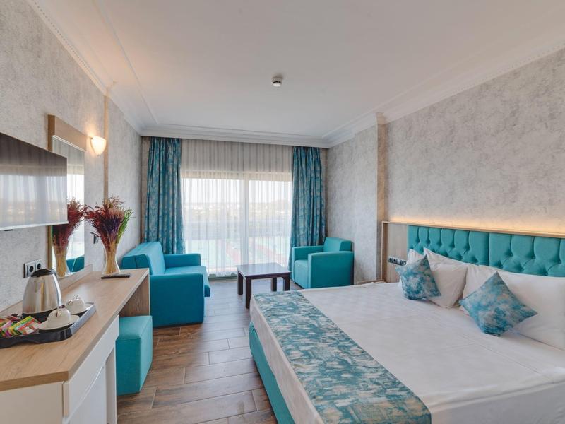 Moderner Hotelzimmer mit großem Bett, türkisfarbenen Akzenten, zwei Sesseln und großem Fenster.