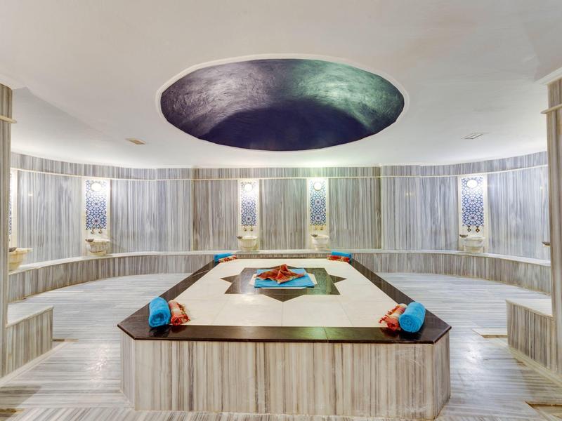 Eleganter Hamam mit hellen Marmorwänden, zentralem Becken und rundem Sternenhimmel an der Decke.