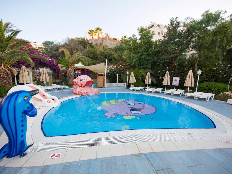 Piscina per bambini all'aperto con giochi d'acqua e sedie a sdraio circondata da alberi.