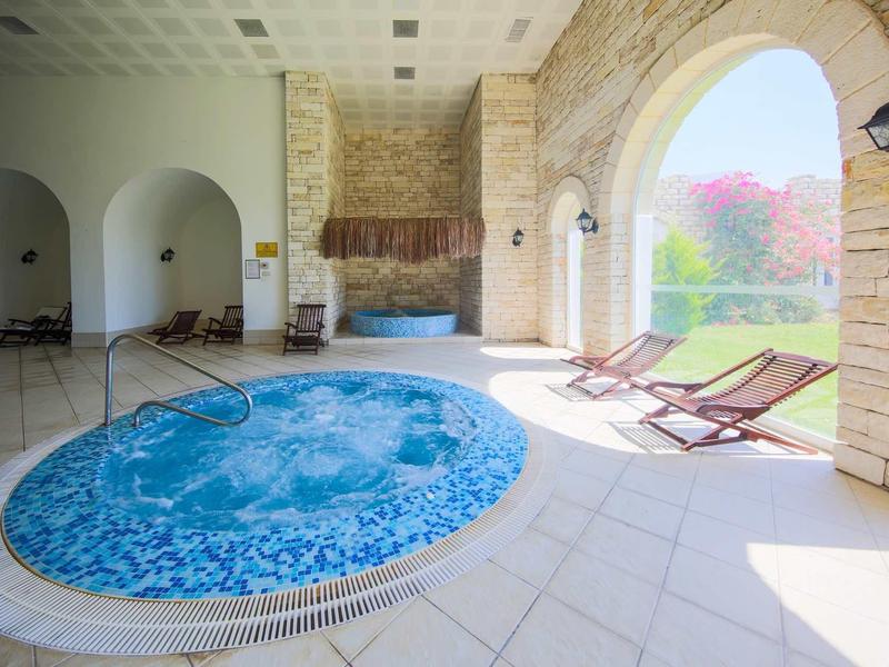 Vasca idromassaggio coperta con due sedie a sdraio vicino a una finestra ad arco con vista sul giardino