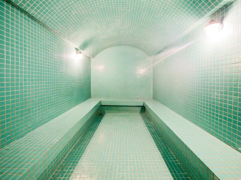 Stanza stretta e lunga con piastrelle verdi e panchine ai lati, illuminata.