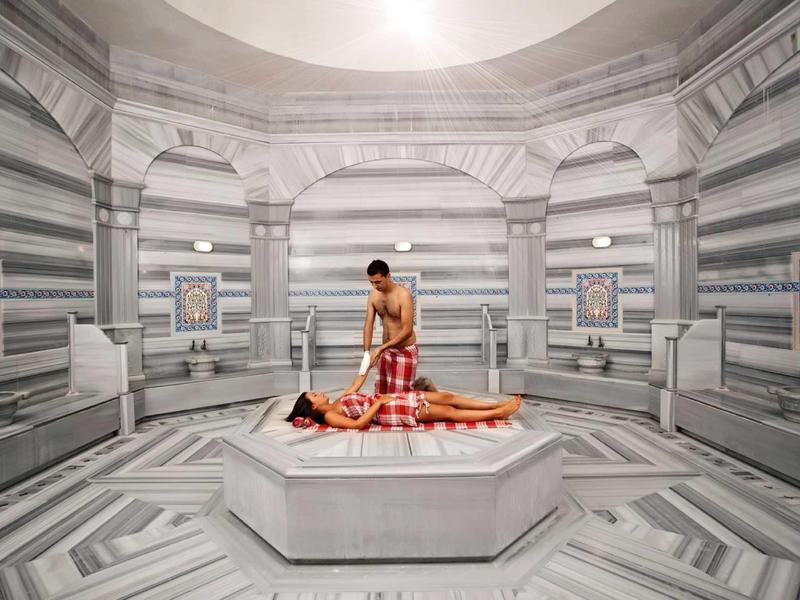 Bagno turco storico con pareti di marmo e massaggio su lastra di pietra riscaldata.