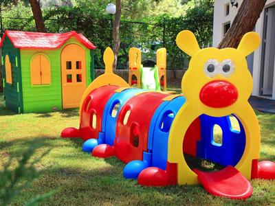 Colorful caterpillar play tunnel and a small green playhouse on grassy playground.