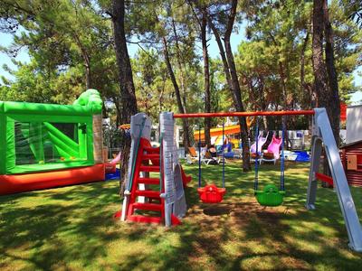 Playground with swings, slide, and bounce house surrounded by trees in a sunny park.