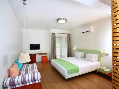 Bright hotel room with double bed, striped sofa, wall TV, and balcony door.