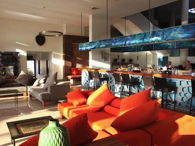 Modern hotel lounge with orange sofas, bar stools, and large windows letting in natural light.